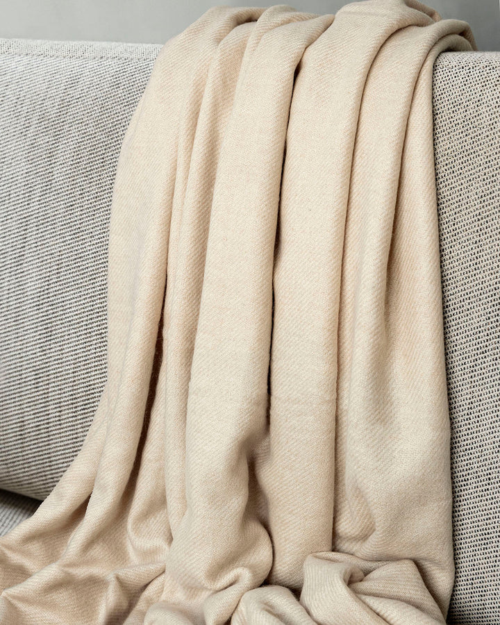 Yakwolle-Decke hängt locker über einer Couche in Creme-beige.