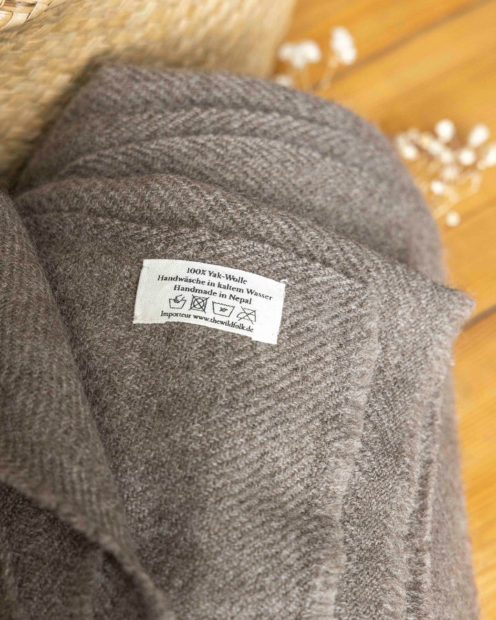Label mit Waschanleitung auf einer zusammengerollten YakWolle-Decke.