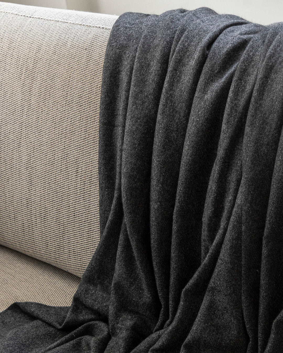 Anthazit farbener Yak-Wolldecke liegt über einer Couch.